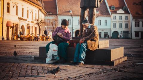 Älteres Pärchen sitzt am Sockel einer Statue und trinkt Cola auf einem Marktplatz in Sibiu, Rumänien