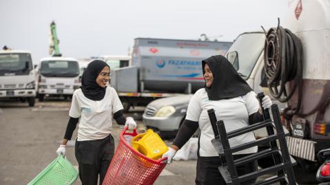 Two women carrying utensils to clean up trash at the beach